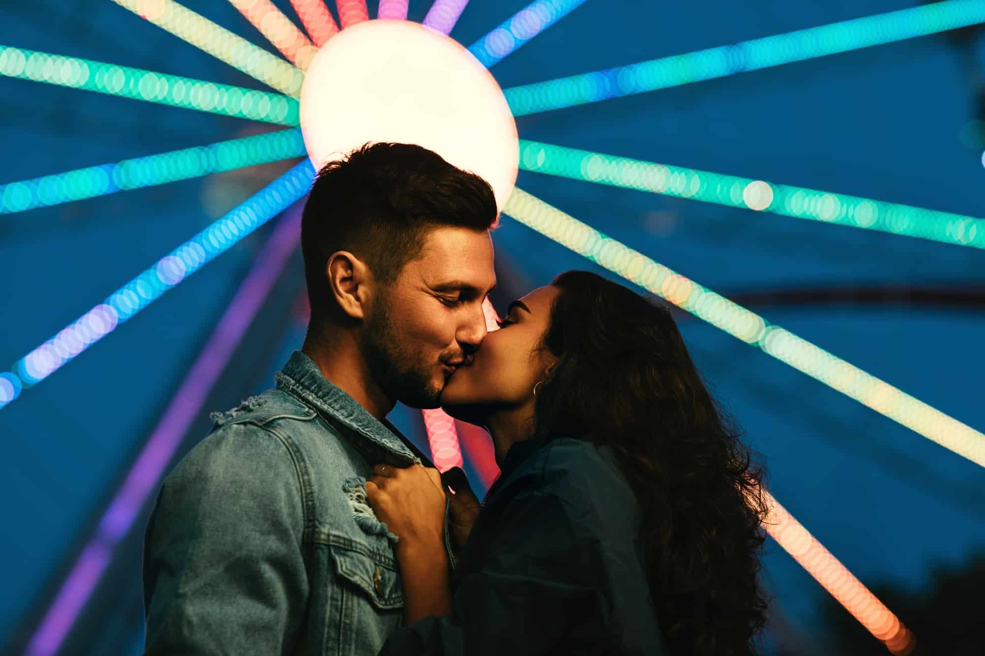 Young couple kissing in front of a Ferris wheel