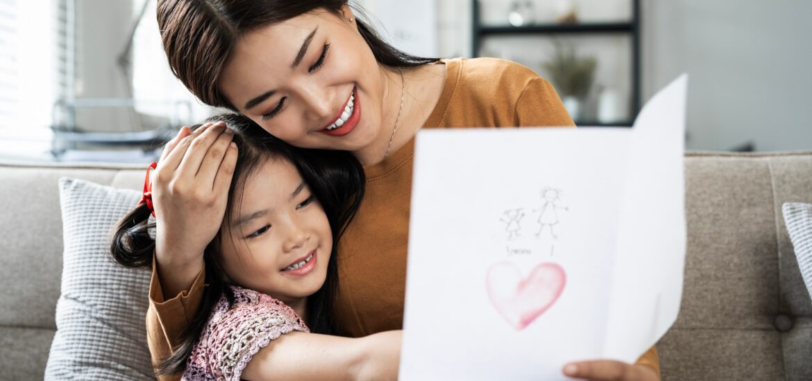 Child daughter is congratulating mom and giving her postcard. Mum and girl smiling and hugging.