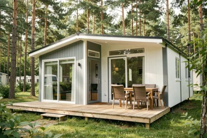 Extérieur moderne d'un mobil-home haut de gamme avec terrasse en bois et grandes baies vitrées entouré de pins dans un camping verdoyant